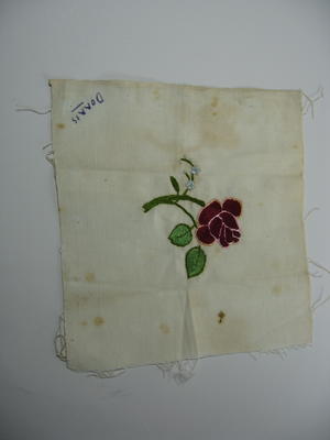Square, cream cloth with embroidered red rose and 'Dorris' written in one corner.