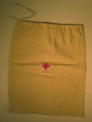 Small drawstring bag made of calico, with a label sewn on the front: 'Gift of the British Junior Red Cross'