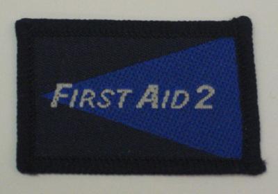 Navy and blue cloth flash, to be worn on uniform by Red Cross Junior who holds a certificate in First Aid. With the words 'First Aid 2' in white.