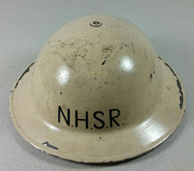 Oval cream coloured hard hat featuring the letters N.H.S.R. to front and back. The interior is of soft leather and has a strap to tighten under chin.
