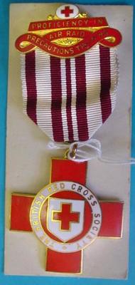 Red/white and gold coloured badge with red cross pendant hanging from ribbon. Ribbon is white with 5 vertical dark red lines. Top piece features a red cross and gold text on red background.