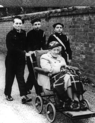 Three male Junior Red Cross cadets with an elderly lady in a wheelchair