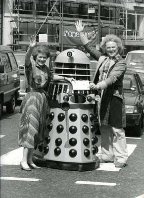 Sue MacGregor and Colin Baker and holding a 'For Sale' sign next to a Dalek from the Dr Who television series