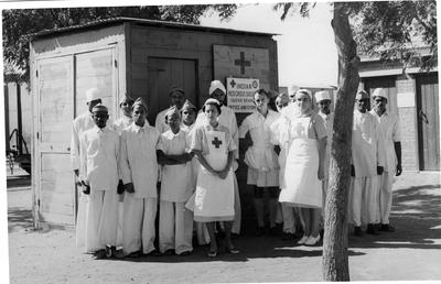 Red Cross personnel near sign featuring Red Cross and St John emblems with text 'Indian Red Cross Society (Sudan Branch) Office and Supplies'