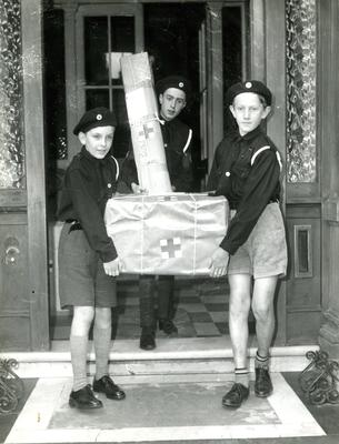 Black and white photograph. Cadets carrying parcels of supplies to waiting vehicles, then to aircraft for Persia