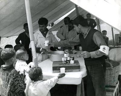 Black and white photograph. Milk distribution station for Algerian refugees at Beni Drar, children and Red Cross team under a tent.