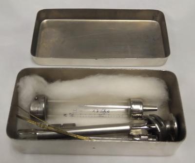 A syringe and surgical needles in a chrome box