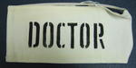 White cotton brassard with DOCTOR printed in black stencilled letters. Fastened with elastic.
