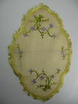 Yellow cloth with fringing on scalloped edges and decorated with embroidered purple flowers.