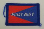 Red and blue cloth flash, to be worn on uniform by Red Cross Youth who holds a certificate in First Aid 1. With the words 'First Aid 1' in white.