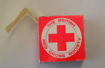 Cardboard box containing a roll of stickers. Each sticker is circular with the words 'The British Red Cross Society' around the emblem.