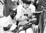 A British Red Cross nurse spoon feeds a Kenyan child as his mother watches on
