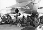 Wounded soldiers seated under a plane with a Red Cross emblem