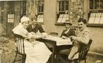 VAD member [Dorothy Hancock] in nursing uniform sitting at a table playing cards with male [patients] at [Southmead Hospital, Bristol]