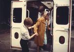 Colour photograph of Red Cross Youth members helping an elderly lady out of an ambulance